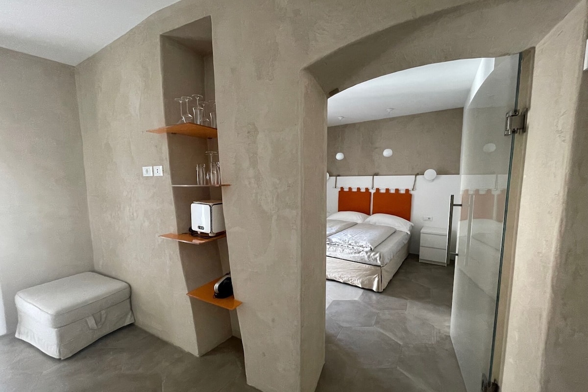 Ein modernes Schlafzimmer mit Bett, Nachttisch, Kleiderschrank und einer integrierten Ablage mit Gläsern und Toaster.