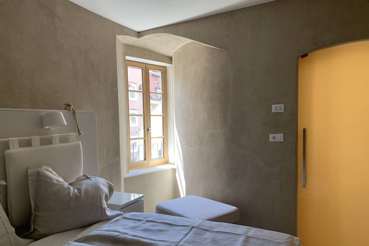 Ein Schlafzimmer mit Bett, Nachttisch, Lampe, Fenster und Tür.