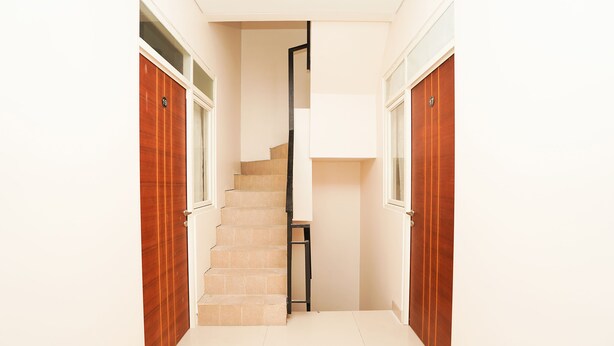 A narrow hallway with a wooden door on the left and a wooden door on the right, leading to a staircase. - Hotel O Menjangan Residence at Citraland 1 (Surabaya)