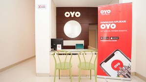 A reception area with a desk, two green chairs, a large OYO Hotels sign, and a promotional banner for the OYO app. - Hotel O Menjangan Residence at Citraland 1 (Surabaya)