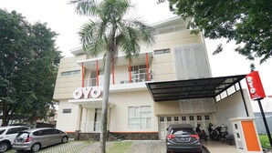 A modern building with a 'YOYO' sign, a covered parking area, and several parked cars and motorcycles. - Hotel O Menjangan Residence at Citraland 1 (Surabaya)