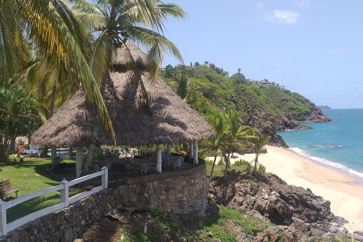 A beachside resort with thatched-roof structures, a white fence, and a view of the ocean.