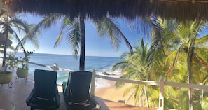A beach view with two lounge chairs, a thatched roof, and palm trees. - Bungalows Lydia (San Francisco)