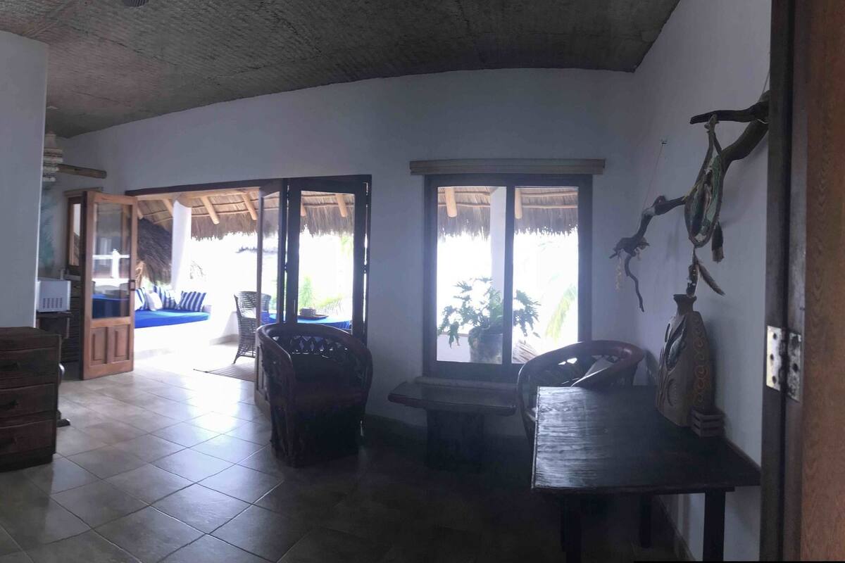A room with a bed, a dresser, a lamp, and a view of an outdoor area with a thatched roof.