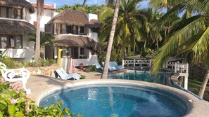 A pool area with lounge chairs, a thatched-roof structure, and palm trees. - Bungalows Lydia (San Francisco)