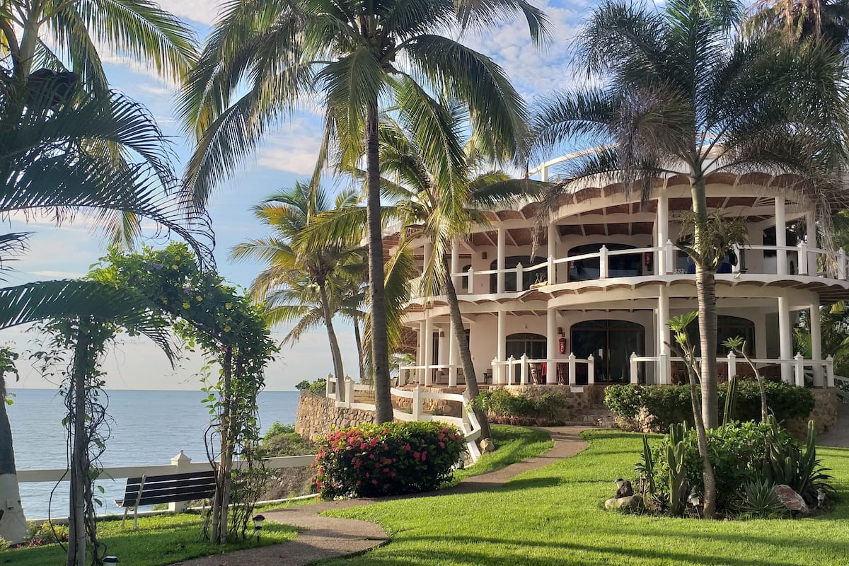 A multi-story hotel with a balcony, surrounded by palm trees and a view of the ocean.