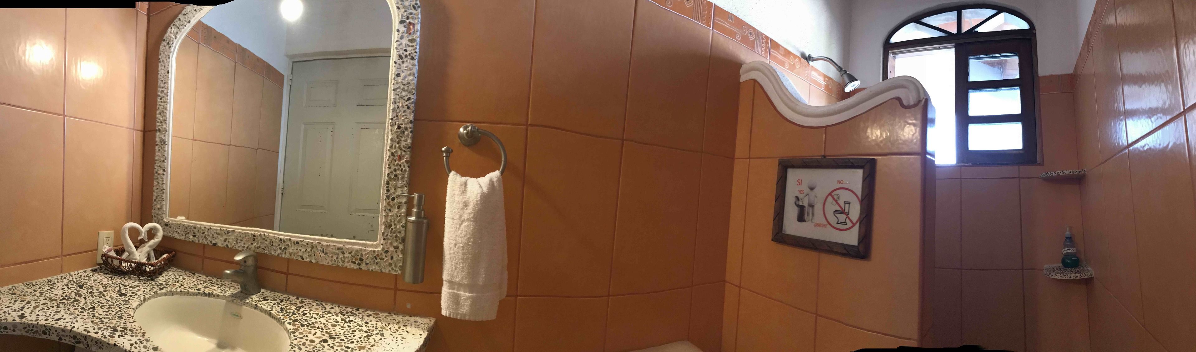 A bathroom with a sink, mirror, towel rack, and a sign indicating no toilet paper use.