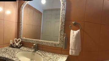 A bathroom with a sink, mirror, towel rack, and a sign indicating no toilet paper use.
