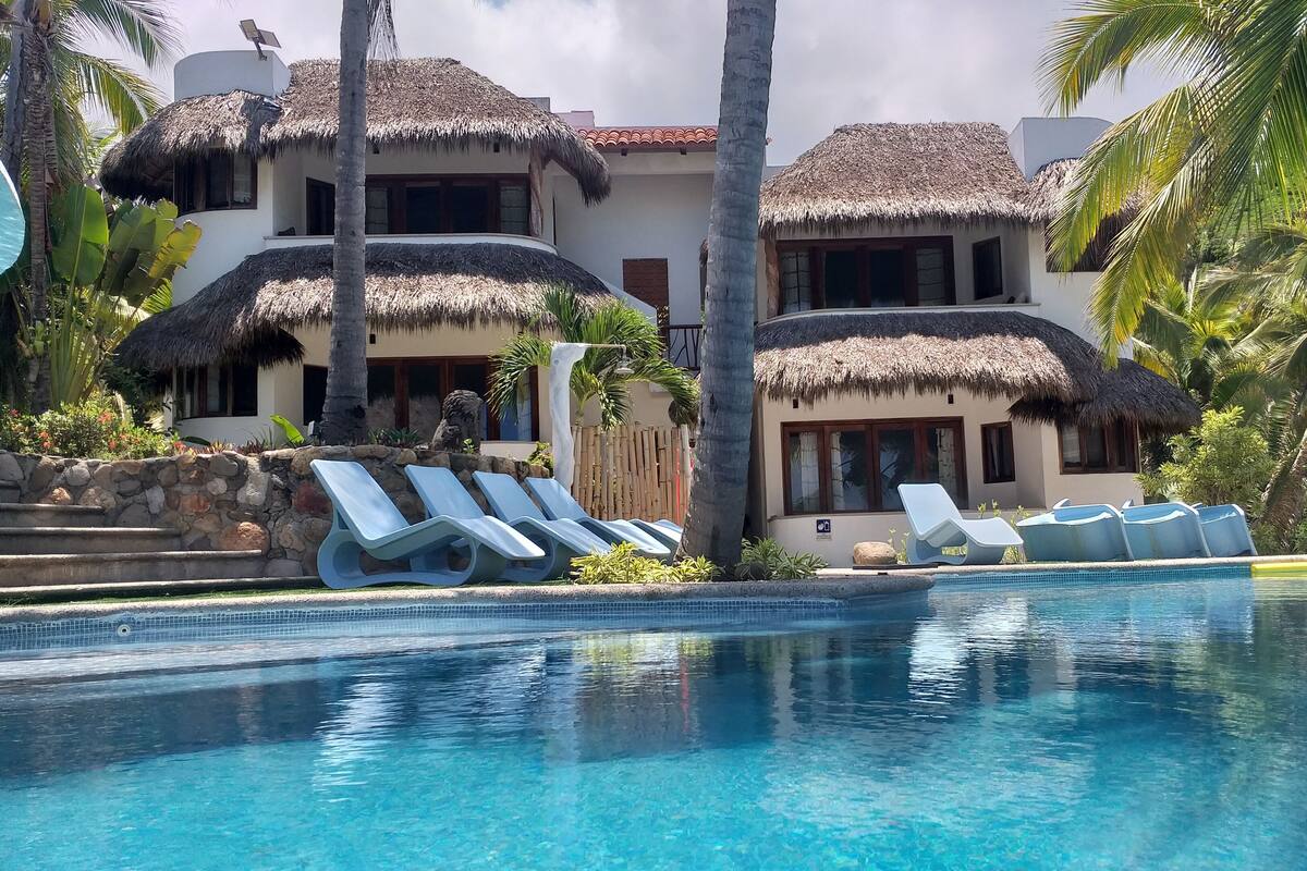 A resort with a pool, thatched-roof buildings, and lounge chairs.