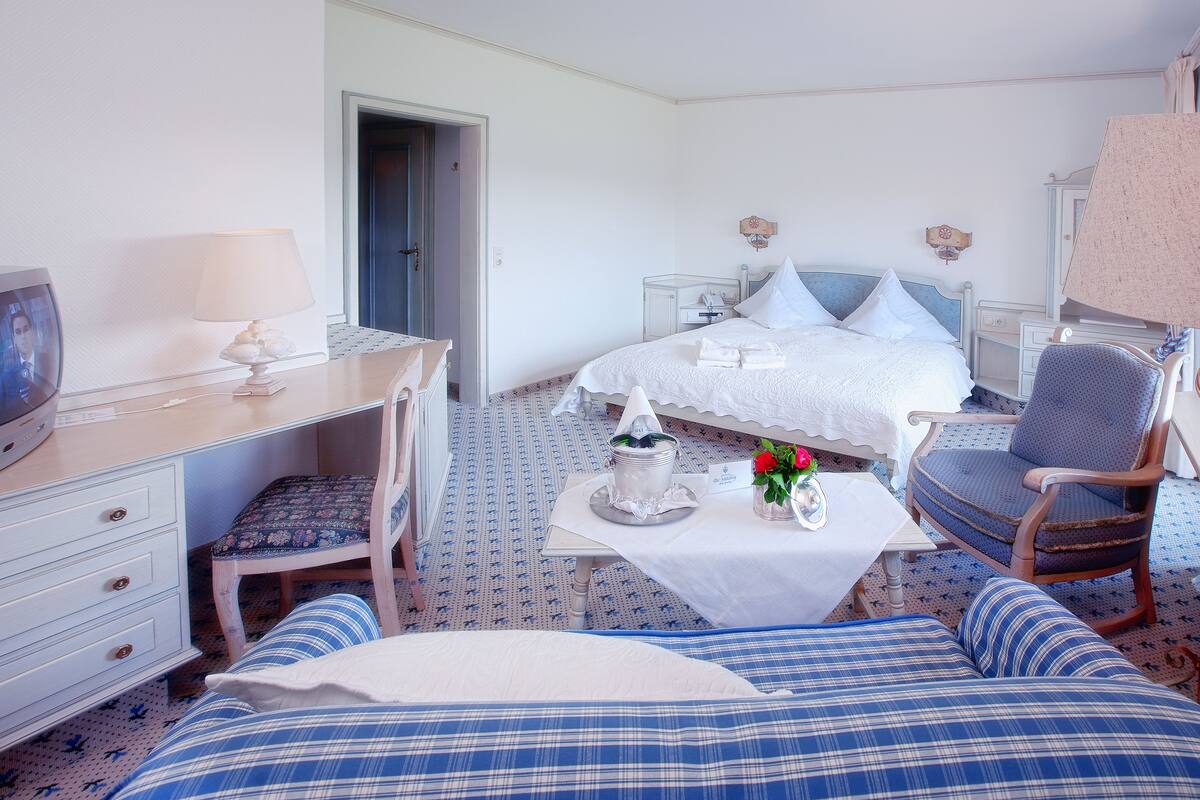 Habitación de hotel con cama, escritorio, silla, mesita con un florero y televisor.