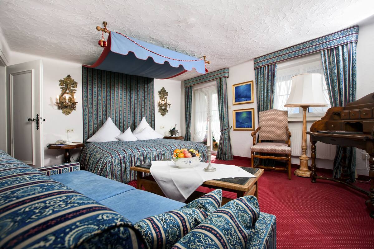 Habitación de hotel con una cama grande, un sofá, un piano de madera y una mesa de comedor con frutero.