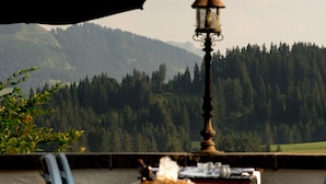 Un patio con vista a una montaña boscosa, una fuente de agua y mobiliario exterior.