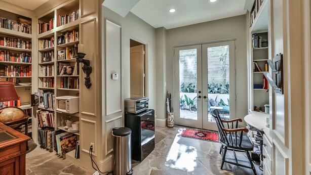 A spacious living room with a large bookshelf, a dining area with a table and chairs, and a sliding glass door leading to a patio. - Artist’s Library; Private Swimming Pool in River Oaks Area (Houston)