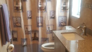 A small bathroom with a toilet, sink, and shower curtain featuring lighthouse designs. - Beautiful home in the quiet neighborhood (Coral Springs)