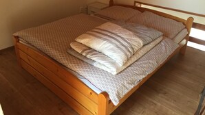 Un letto in legno singolo con una coperta a motivi e cuscini in una stanza con pavimento in legno e soffitto spiovente.