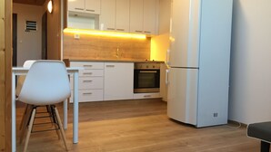 Una cucina compatta con mobili bianchi, forno integrato e frigorifero bianco.