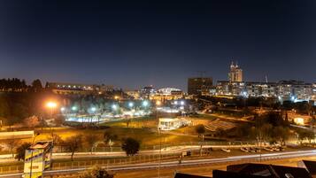Paisaje urbano nocturno con edificios iluminados, un estadio y una autopista con estelas de luz.