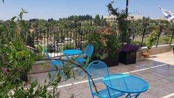 A terrace with blue metal chairs and a table, surrounded by potted plants and flowers.