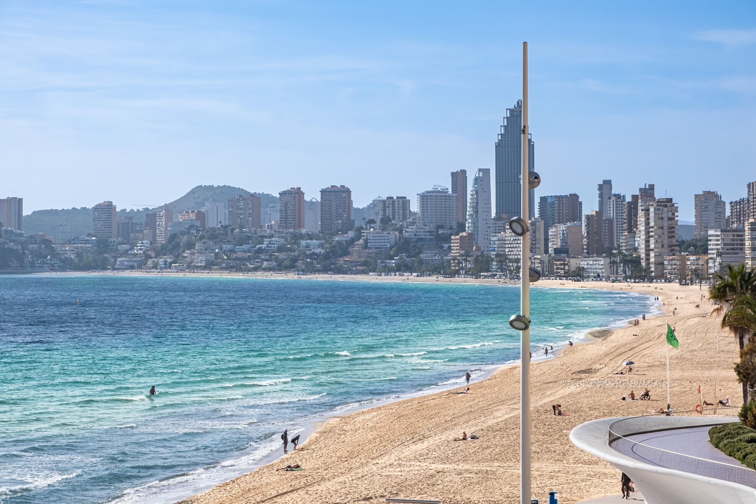 A beach with a city skyline in the background, a sandy beach, and a curved structure near the water.