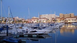 A marina with numerous boats docked, a large building in the background, and calm water reflecting the boats. - UNFINY APARTMENT by the sea (QUARTEIRA)