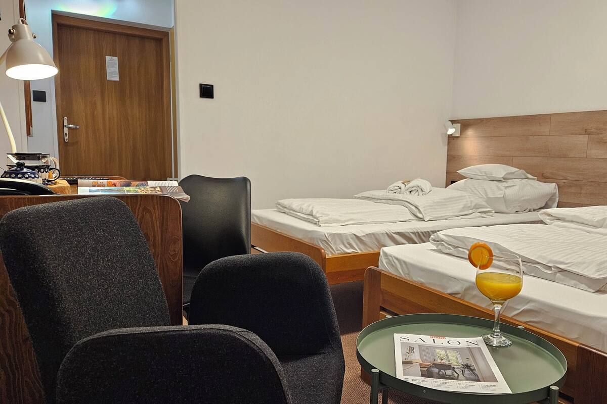 A hotel room with two beds, a desk with a lamp, a chair, and a small table with a magazine.