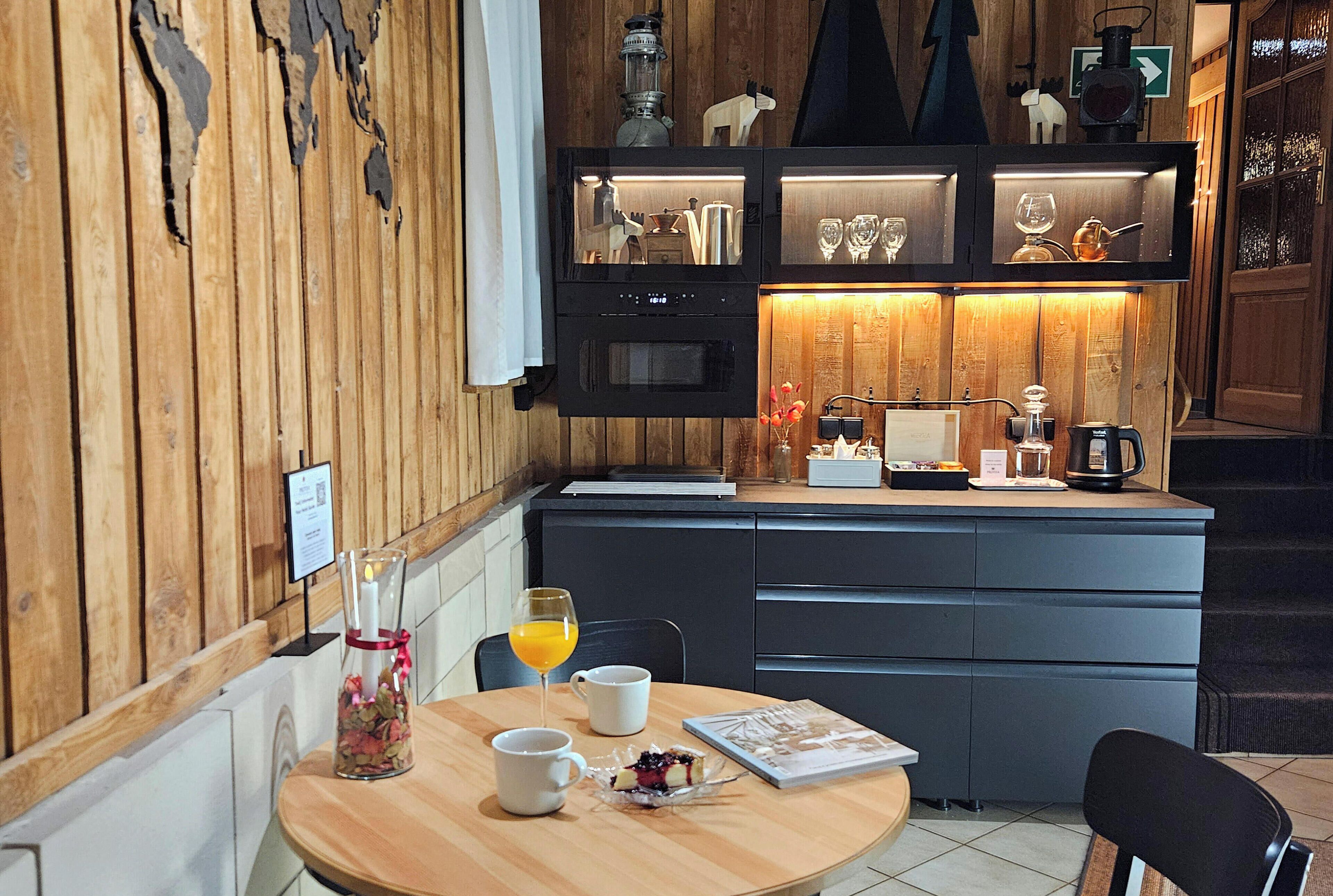 Een kamer met houten lambrisering, een eettafel gedekt voor twee personen, een koffiezetapparaat en een klein keukentje met kastjes en een koelkast.
