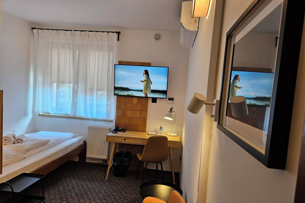 A hotel room with a bed, a desk, a chair, a TV, and a window with curtains.