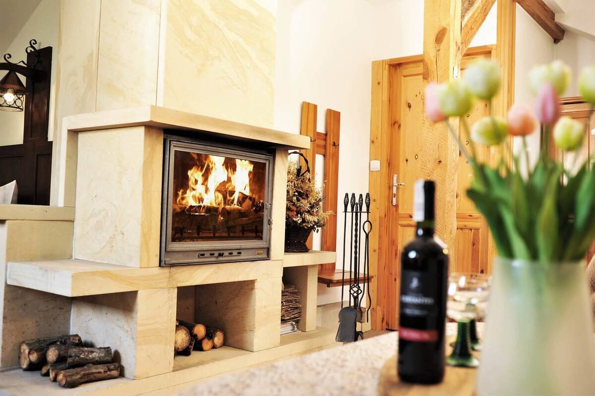 A cozy room with a wood-burning stove, a vase with flowers, and a bottle of wine on a table.