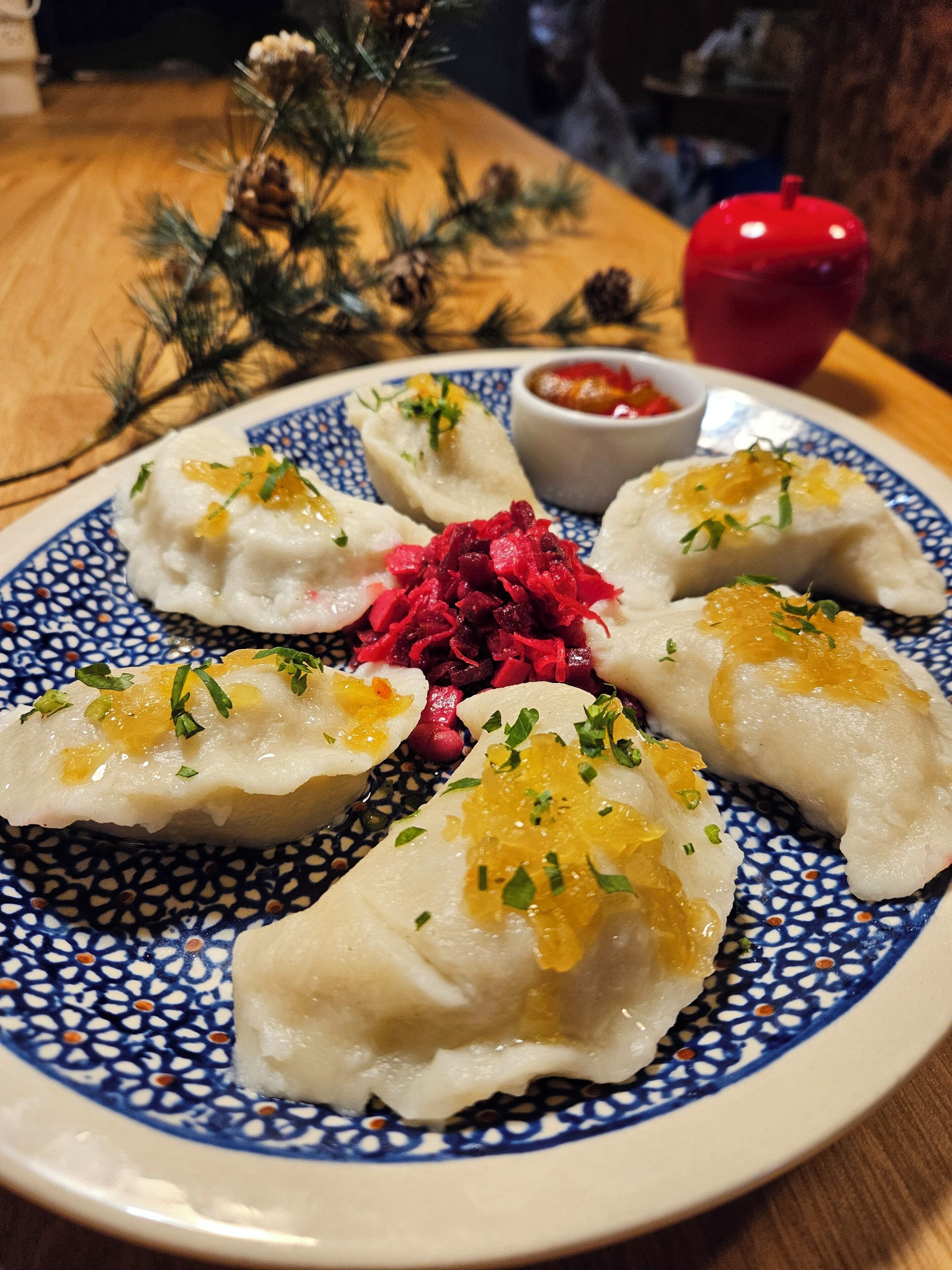 A plate of dumplings with a side of beetroot salad and a small bowl of sauce.