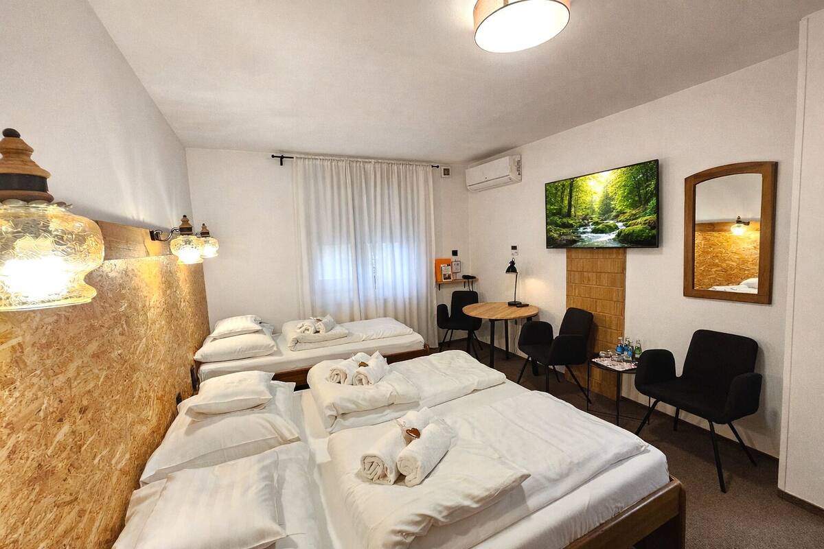 A hotel room with multiple beds, a TV, a desk, and chairs.