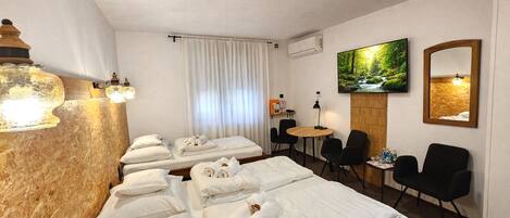Une chambre d’hôtel avec plusieurs lits, une télévision, un bureau et des chaises.