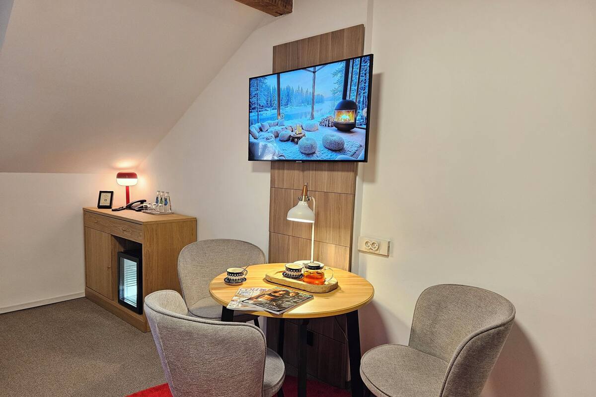 A cozy room with a TV mounted on the wall, a wooden cabinet, a round table with chairs, and a red carpet.