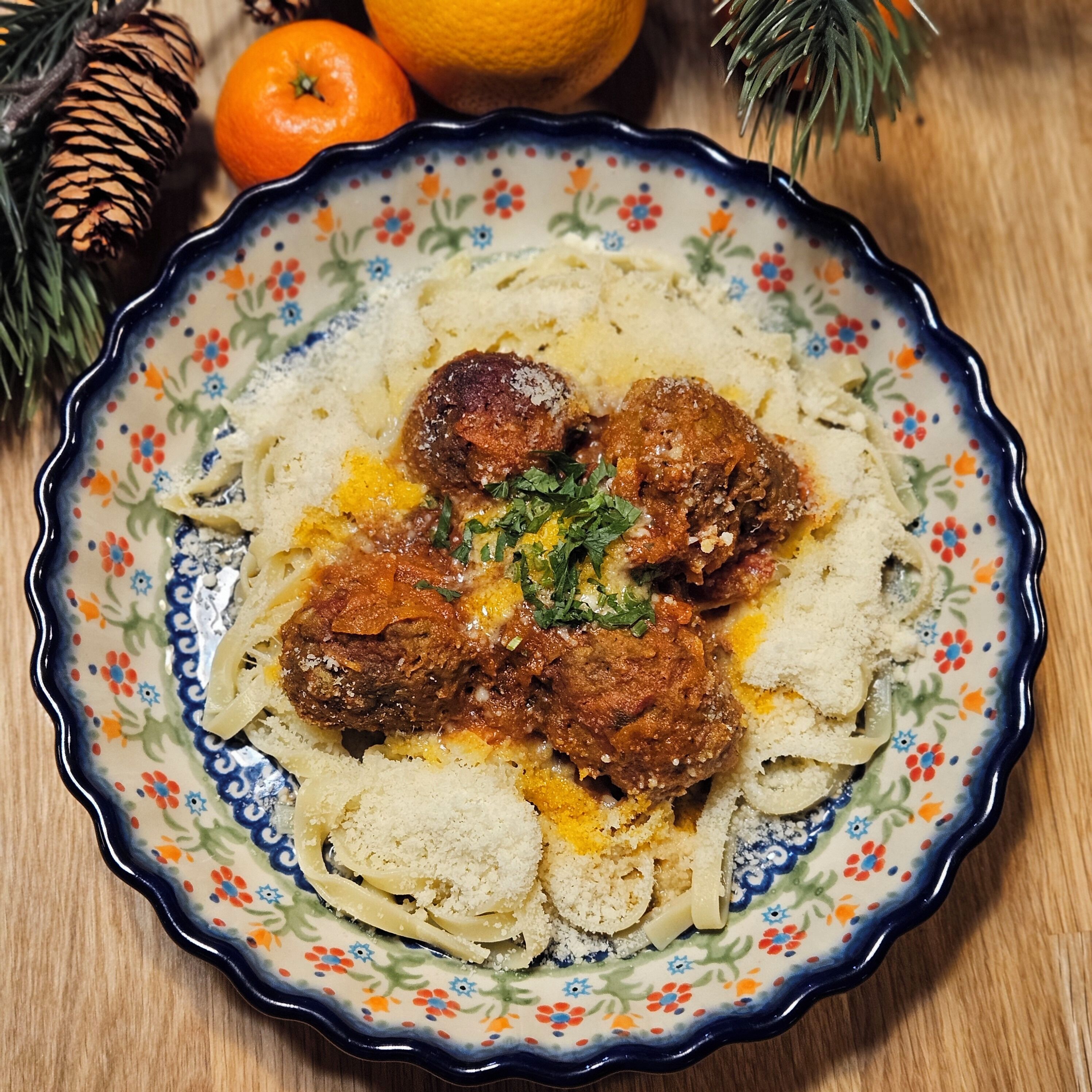 A plate of food with meatballs and pasta, placed on a decorative plate with a floral pattern.