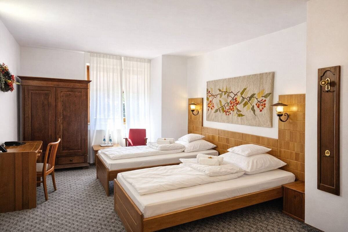 A hotel room with two single beds, a wooden desk, a chair, a wardrobe, and a painting on the wall.