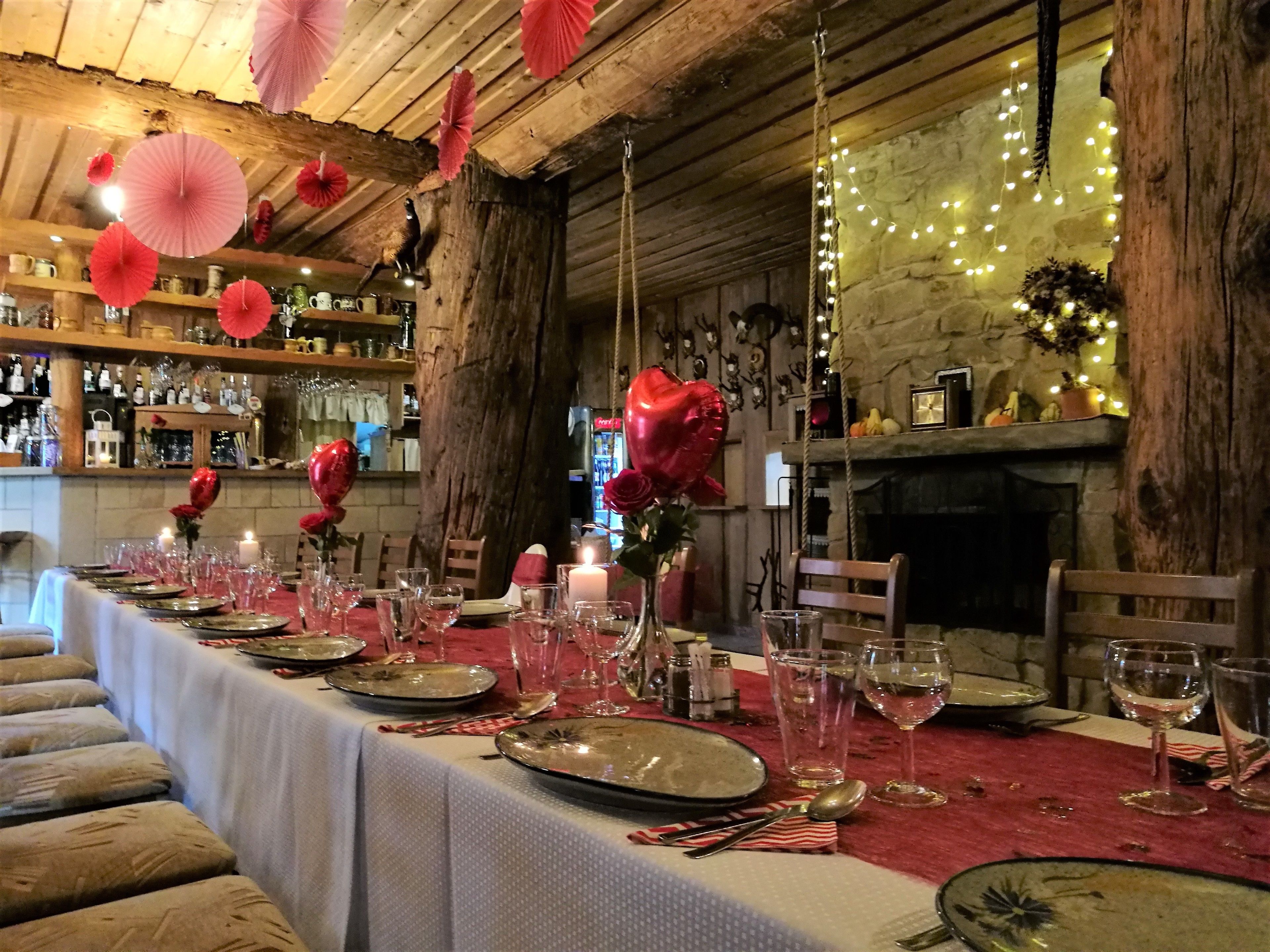 A long dining table set with plates, glasses, and candles, decorated with red roses and hanging paper fans.