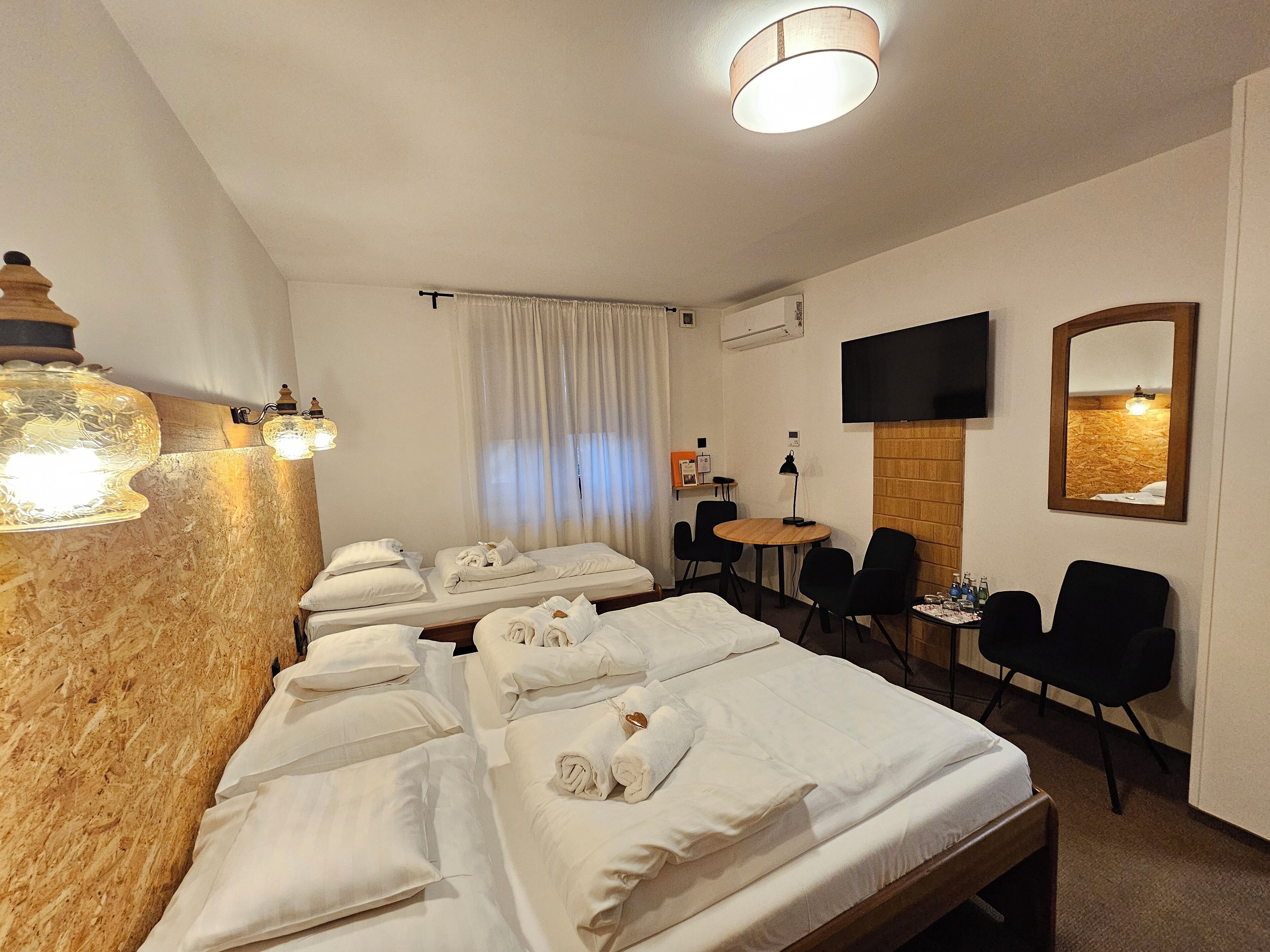 Una habitación de hotel con varias camas, televisión, espejo, una mesita y sillas.