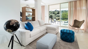 Un salon moderne avec un canapé d’angle, un globe terrestre posé sur un trépied, un pouf à motifs et une vue sur un balcon aménagé avec du mobilier d’extérieur.