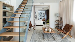 Un salon moderne avec un escalier, une table basse avec des livres, un canapé et un fauteuil.