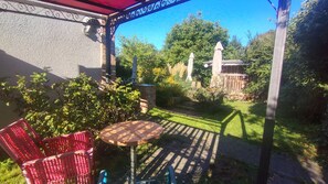 Une terrasse avec une table et des chaises, entourée de verdure et d’un mur en pierre.