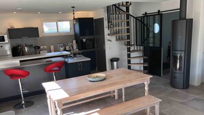 A modern kitchen with a central island, red bar stools, a wooden bench, and a black spiral staircase. - ILE TUDY - Contemporary house 6 places with garden 100m from the beach (Île-Tudy)