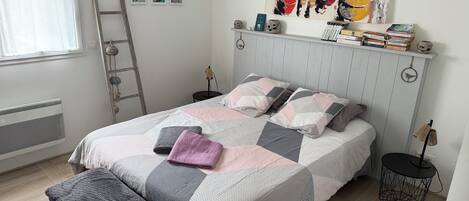 A neatly arranged bedroom with a bed, bedside tables, a ladder, and a wall with artwork.
