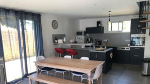 A modern kitchen with a wooden dining table, red bar stools, and a built-in island with a sink. - ILE TUDY - Contemporary house 6 places with garden 100m from the beach (Île-Tudy)