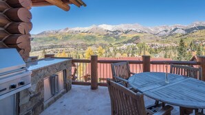 Une terrasse en bois avec un barbecue en pierre, une table et des chaises, offrant une vue sur un paysage montagneux.