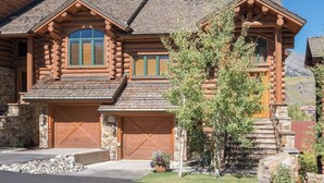 A log cabin with a stone foundation, a large garage, and a prominent window. - Townhomes On The Creek 119 (Mountain Village)