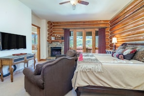 A bedroom with a bed, a television, a fireplace, and a view of the outdoors.