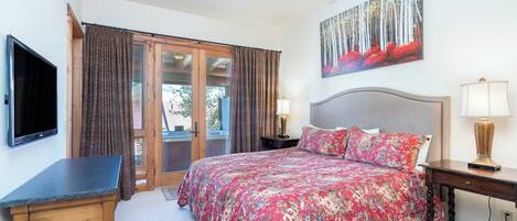 A bedroom with a bed, a desk, a television, a ceiling fan, and a painting on the wall.