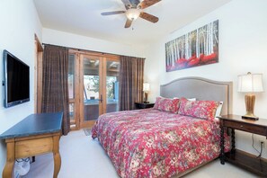 A bedroom with a bed, a desk, a television, a ceiling fan, and a painting on the wall.