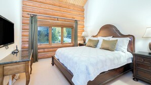 A log cabin bedroom with a bed, a desk, a television, and a window with curtains. - Townhomes On The Creek 119 (Mountain Village)