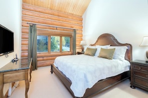 Une chambre située dans un chalet en rondins, avec un lit, un bureau, une télévision et une fenêtre avec des rideaux.