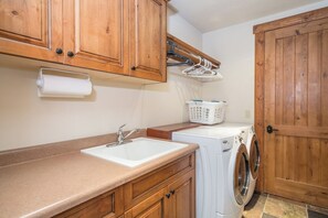 A laundry area with a sink, washing machine, wooden cabinets, and a door.